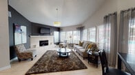 This single-floor lounge in Jacksonville, Florida, offers a well-appointed and versatile gathering space with a thoughtful layout and modern design elements throughout. The main living area commands attention with its vaulted ceiling, a bold dark accent wall, and a tile-surround fireplace flanked by accent chairs. A drum pendant light anchors the space, while large windows dressed with blinds and grommet curtains flood the room with natural light. Light tile flooring extends throughout, complemented by a rich, textured area rug and a round glass coffee table. Ample seating, including a neutral-toned sofa with gold and striped accent pillows, creates an inviting atmosphere for socializing.

Adjacent to the living area, a dining section features a dark wood table and chairs set beneath soaring ceilings, with a large abstract canvas artwork adding a creative focal point. A sideboard with a coffee station completes this zone.

The kitchenette is well-equipped with dark cabinetry, granite countertops, stainless steel appliances including a full refrigerator and microwave, and a breakfast bar with upholstered counter stools. A glass-paneled door and flanking windows provide direct views of an outdoor pool area, seamlessly connecting the interior to the exterior environment.