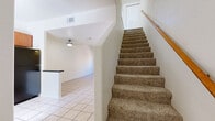 Located in Mesa, AZ, this two-story home offers a practical and well-organized layout across two floors. The main level features light tile flooring throughout the open living, dining, and kitchen areas. The kitchen is equipped with warm-toned wood cabinetry, dark countertops, a breakfast bar, and black appliances including a refrigerator, range, and over-the-range microwave. The living area is bright and airy, with a ceiling fan and sliding glass doors that open to a private patio, allowing natural light to fill the space. A carpeted staircase with a wood handrail connects the two levels. Upstairs, both bedrooms are carpeted and feature ceiling fans and generous closet space, including walk-in and sliding-door closets. The primary bedroom is comfortably sized and includes ample storage. Both bathrooms feature wood-look flooring, vanities with mirrored medicine cabinets, and one includes a full tub-shower combination. Additional highlights include an in-unit laundry area, multiple closets throughout, and a hallway connecting the upper-level rooms. The neutral color palette and clean finishes create a bright, move-in-ready atmosphere suited for comfortable everyday living.