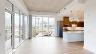 This two-story residence offers a well-organized layout across two floors, combining modern industrial design with clean, contemporary finishes. Exposed concrete ceilings are a defining architectural feature throughout, adding an urban character that contrasts with the bright white walls and light-toned hardwood flooring found in every room.

The lower level houses the kitchen and a living area. The kitchen is a standout space, featuring gray two-tone cabinetry, stainless steel appliances, a subway tile backsplash, and a large central island with a white quartz countertop illuminated by glass pendant lights. Floor-to-ceiling sliding glass doors in the adjacent living area flood the space with natural light and provide views of the surrounding outdoor scenery.

The upper level, slightly larger than the lower, contains the three bedrooms, including a generously sized primary suite. The primary bedroom connects to a well-appointed bathroom featuring a glass-enclosed shower, a soaking tub, and tile surround. A spacious walk-in closet with built-in shelving and hanging rails provides substantial storage. Additional bedrooms are bright and well-proportioned, each benefiting from large windows with scenic outdoor views. Five bathrooms in total are distributed across both floors, finished with neutral tile and modern fixtures throughout.