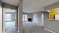 This single-floor residence offers a thoughtfully designed layout that balances comfort and functionality. The living room serves as the centerpiece of the home, featuring a tile-surround fireplace and neutral gray walls that create a calm, inviting atmosphere. Plush wall-to-wall carpeting extends throughout the main living areas and bedrooms, adding warmth underfoot. French doors in the living area welcome an abundance of natural light and provide access to the outdoors.

The kitchen is efficiently arranged in an open-concept style, accessible via a peninsula that connects it to the main living space. Warm honey-toned wood cabinetry lines the walls, paired with light stone countertops, a gas range with overhead ventilation, and a full-size refrigerator. The wood-look flooring in the kitchen adds a practical contrast to the carpeted areas.

The bedrooms are generously proportioned, each featuring wide windows that let in natural light and views of the surrounding greenery. Closet space is well accommodated, with double-door closets offering built-in shelving for organized storage.

The two bathrooms are cleanly finished with light cabinetry, vanity mirrors, and warm wood-look flooring. One bathroom includes a tub-shower combination with white tile surround, while the other features a more compact layout. The overall palette of soft grays and whites gives the entire residence a cohesive, understated aesthetic.