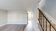 Located at 809 Dozer Dr in West Jefferson, Ohio, this two-story home offers a thoughtfully organized layout spread across two well-proportioned floors. The main level features a combined kitchen and living area, where the galley-style kitchen stands out with white shaker cabinetry, dark granite-look countertops, stainless steel appliances, and durable wood-look flooring. Natural light enters through a decorative fanlight above the front entry door, creating a welcoming atmosphere. The open living area flows seamlessly from the kitchen, maintaining a clean, neutral palette throughout. A dedicated laundry area on the main level includes a full-size washer and dryer with overhead shelving for added storage convenience. A carpeted staircase with a sleek black metal railing leads to the upper floor, where three bedrooms are situated. The spacious primary bedroom provides a comfortable retreat, while the additional bedrooms offer plush carpet flooring and natural light from windows with blinds. One bedroom features a sliding closet with built-in railing for organized storage. Throughout the home, textured ceilings, soft gray walls, and crisp white trim create a clean, move-in-ready aesthetic. A central hallway connects the upper-level rooms efficiently.
