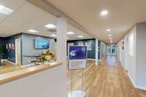 Located at 42 Cedar Pond Dr in Warwick, Rhode Island, this well-appointed single-story community facility spans a generous footprint across four distinct areas, each designed to support an active and social lifestyle.

The entry reception area sets a welcoming tone with hardwood-style flooring, a reception counter, wall-mounted display, and a bright corridor leading deeper into the facility. Artwork and signage throughout reinforce a clean, community-oriented aesthetic.

The standout feature of the space is the expansive fitness center, divided into two zones. The main gym area is dramatic in scale, boasting soaring vaulted ceilings, bold cobalt-blue accent walls, and a striking floor-to-ceiling window wall that floods the space with natural light and frames outdoor greenery. This area is outfitted with a comprehensive array of cardio equipment, including treadmills and stationary bikes, alongside strength machines and free weights. Globe pendant lighting adds a modern design touch. Full-length mirrors enhance the sense of space throughout the fitness floor.

A comfortable lounge area features warm hardwood flooring, a fireplace, lounge seating, a billiards table, and a wall-mounted television, creating an inviting space for relaxation. Adjacent to this is a collaborative common area with high-top tables and additional seating, well-lit by recessed and panel lighting against deep teal accent walls adorned with colorful artwork.