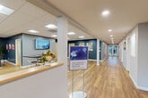 Located at 42 Cedar Pond Dr in Warwick, Rhode Island, this well-appointed single-story community facility spans a generous footprint across four distinct areas, each designed to support an active and social lifestyle.

The entry reception area sets a welcoming tone with hardwood-style flooring, a reception counter, wall-mounted display, and a bright corridor leading deeper into the facility. Artwork and signage throughout reinforce a clean, community-oriented aesthetic.

The standout feature of the space is the expansive fitness center, divided into two zones. The main gym area is dramatic in scale, boasting soaring vaulted ceilings, bold cobalt-blue accent walls, and a striking floor-to-ceiling window wall that floods the space with natural light and frames outdoor greenery. This area is outfitted with a comprehensive array of cardio equipment, including treadmills and stationary bikes, alongside strength machines and free weights. Globe pendant lighting adds a modern design touch. Full-length mirrors enhance the sense of space throughout the fitness floor.

A comfortable lounge area features warm hardwood flooring, a fireplace, lounge seating, a billiards table, and a wall-mounted television, creating an inviting space for relaxation. Adjacent to this is a collaborative common area with high-top tables and additional seating, well-lit by recessed and panel lighting against deep teal accent walls adorned with colorful artwork.