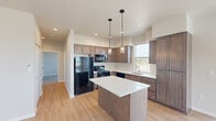 Located at 920 E Fourth Ave in Post Falls, Idaho, this single-floor unit offers a contemporary, thoughtfully designed layout that balances functionality with modern aesthetics. The open-concept kitchen serves as the heart of the space, showcasing rich medium-toned wood cabinetry, crisp white quartz countertops, and a central island illuminated by two stylish pendant lights. Black Whirlpool appliances—including a refrigerator, range, microwave, and dishwasher—complement the kitchen's clean design. Light-toned hardwood flooring flows throughout the main living areas, adding warmth and continuity, while recessed lighting enhances the bright, airy atmosphere.

The living area extends toward a sliding glass door that opens to a private balcony, offering elevated outdoor views of the surrounding Post Falls neighborhood. Multiple windows throughout the unit invite generous natural light. Bedrooms are carpeted for comfort, with neutral tones and ample closet storage featuring sliding doors and built-in rods. One bedroom includes a wall-mounted mini-split unit for independent climate control. The overall ambiance is clean, modern, and move-in ready, with a neutral color palette that complements a variety of interior styles.