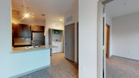 This single-story apartment combines functional design with modern finishes throughout its thoughtfully arranged floor plan. The kitchen features stainless steel appliances, including a full-size refrigerator, and is anchored by a peninsula with a light granite-style countertop that provides additional workspace and casual seating. Rich dark cabinetry offers generous storage, while a sink positioned on the peninsula enhances the kitchen's usability.

Wood-style flooring runs through the main living areas, lending warmth and continuity to the space. A hallway connects the primary areas and leads to the bedroom, which is finished with carpet for added comfort underfoot. The unit includes a dedicated in-unit laundry area with a full-size washer and dryer, a notable convenience tucked neatly into its own alcove along the hallway. Neutral white walls and recessed lighting throughout keep the space feeling bright and clean. Gray interior doors and coordinated trim details provide a cohesive, contemporary aesthetic. The single-floor layout ensures easy accessibility and a streamlined living experience.