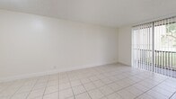 Located in Lauderdale Lakes, Florida, this single-level 2-bedroom, 2-bathroom residence offers a practical and well-organized layout. Light-tone ceramic tile flooring runs consistently throughout the home, creating a cohesive and easy-to-maintain interior. The living room is generously sized, featuring a textured ceiling and vertical blind-covered windows that allow natural light to filter in. Adjacent to the living area, a dedicated dining space connects seamlessly to the kitchen via a pass-through window, enhancing the open feel of the common areas. A hallway links the main living spaces to the bedrooms, each of which features windows with outdoor views of the surrounding greenery and neighborhood. The spacious primary bedroom offers ample room for furnishings, while the second bedroom provides similar brightness and versatility. Two closets offer practical storage throughout the unit. The bathrooms serve each bedroom's needs: one features a full tub-shower combo with white tile surround and striped curtain, while the second includes a vanity with dark granite countertop, white cabinetry, and a vessel sink. Overall, the home presents a clean, bright, and functional living environment well-suited for comfortable Florida living.