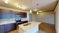 This single-floor residence offers a thoughtfully designed open-concept layout that seamlessly connects the kitchen, dining, and living areas. The kitchen is a standout feature, showcasing rich dark-wood cabinetry, a glass tile backsplash, stainless steel appliances including a refrigerator, range, and built-in microwave, and a large center island with a quartz-style countertop and double undermount sink. Pendant lighting and track lighting illuminate the space, while light hardwood flooring runs throughout the main living areas, adding warmth and continuity.

The living and dining areas are open and airy, finished with crown molding and neutral toned walls that contribute to a clean, modern aesthetic. The bedrooms are generously sized, carpeted for comfort, and equipped with ceiling fans. One bedroom offers direct access to a private balcony through glass doors, allowing natural light to flood in and providing views of the surrounding area.

A dedicated in-unit laundry closet houses a full-size washer and dryer, adding everyday convenience. A bathroom with hardwood-style flooring and clean finishes completes the layout. Overall, this residence combines practical functionality with contemporary finishes throughout.