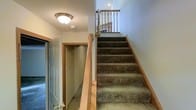 This multi-story home spans three floors, offering a well-organized vertical layout designed for comfortable living. The staircase serves as a central connecting element throughout the home, finished with plush, earth-toned carpeting and complemented by warm wood railings and newel posts that add a classic, inviting character to the interior.

The stairwell is brightened by a ceiling-mounted light fixture, ensuring the transitional spaces between floors are well-lit and welcoming. Clean white walls throughout provide a neutral, versatile backdrop that enhances the sense of openness as you move between levels. Wood-trimmed doorways add a consistent design detail that ties the interior together cohesively.

Adjacent to the staircase, a closet or utility space is accessible, making practical use of the area beneath or beside the stairway. Recessed lighting is also visible on the upper landing, contributing to a layered lighting scheme that extends throughout the home. The overall ambiance is warm and functional, with durable finishes suited for everyday living. The three-floor configuration provides ample opportunity for distinct living, sleeping, and utility zones, making this a spacious and versatile home with a straightforward, approachable design aesthetic.