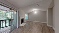 Located at 3200 Oakwood Village Lane in Chamblee, Georgia, this single-floor residence offers a thoughtfully updated interior with a warm, modern aesthetic throughout. The open living area is a standout feature, showcasing dramatic vaulted ceilings with a textured finish that add a sense of spaciousness and architectural character. A classic fireplace anchors the living room, which flows naturally into the dining area beneath a pendant light fixture. Sliding glass doors open onto a private balcony that overlooks a lush, wooded backdrop, providing a serene and natural setting. The kitchen is well-appointed with crisp white cabinetry, granite countertops, stainless steel appliances including an electric range and over-the-range microwave, and a skylight that brings in additional natural light. Wood-look flooring runs throughout the main living spaces, lending a cohesive and contemporary feel. The bedroom offers a generous layout with a window framing views of the surrounding greenery. The bathroom features granite countertops, a tub-shower combination with marble-style tile surround, and brushed nickel fixtures. A dedicated laundry area with a full-size washer and dryer adds everyday convenience to this well-rounded residence.