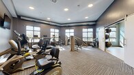 Located at 6620 Chestnut St in Lino Lakes, Minnesota, this fitness center offers a thoughtfully designed, single-floor exercise facility that caters to a wide range of workout needs. The space is divided into two distinct areas: a fully equipped cardio and strength training room, and a dedicated open-floor studio.

The main exercise room features textured carpet tile flooring and is outfitted with a comprehensive selection of equipment, including treadmills, recumbent bikes, elliptical machines, a NuStep cross trainer, and a multi-use strength machine. Multiple flat-screen televisions are mounted on the walls, and recessed lighting illuminates the space throughout. Rows of large windows allow abundant natural light to fill the room, creating an energizing atmosphere. Exposed ductwork along the upper walls adds an industrial design accent.

The adjoining studio area is finished in a calming blue-gray palette with smooth, light-toned hardwood-style flooring ideal for stretching, yoga, or group fitness. A full wall of mirrors maximizes the sense of space and supports movement-based workouts, while a mounted flat-screen television and wall-mounted stability balls and free weights provide additional functionality. Recessed and sconce lighting contribute to a clean, modern aesthetic. Together, the two areas form a versatile and well-appointed fitness facility.