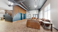 The lobby at 1913 Vine St in Kansas City, Missouri presents a well-appointed single-floor space that balances industrial aesthetics with modern comfort. The main lounge area draws immediate attention with its soaring exposed ceiling, where visible ductwork and pendant Edison-style lighting contribute to an urban industrial character. A striking vertical wood slat accent wall frames a pair of teal elevator doors, creating a bold focal point that anchors the space. Large windows allow natural light to fill the lounge, which is furnished with generous leather sofas and a wood coffee table arranged for comfortable gathering.

Light-toned tile flooring runs throughout, providing a neutral backdrop that unifies the space. An adjacent area serves as a mail and parcel room, featuring a built-in bank of resident mailboxes, a decorative wood-and-slate column detail, and sturdy work tables with gold-accented legs for convenient package handling. A separate utility room provides additional functional space with work surfaces, chalkboard wall accents, and access to support facilities. Together, these areas create a lobby that is both practical and visually engaging, offering residents a polished and welcoming arrival experience in the heart of Kansas City.