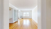 This single-floor unit offers a thoughtfully arranged layout comprising two living areas, a bedroom, bathroom, kitchen, and connecting hallways. Warm-toned hardwood floors extend throughout the main living spaces, lending a cohesive and inviting character to the interior.

The living areas are separated by charming French doors with multi-pane glass panels, allowing natural light to flow between spaces. Large windows fitted with horizontal blinds illuminate the rooms and frame views of the surrounding exterior. Classic crown molding and clean white walls contribute to a timeless aesthetic, while cast-iron radiators provide both functional heating and a nod to the building's architectural heritage.

The bedroom offers a comfortable footprint, featuring hardwood floors, a dedicated closet with built-in shelving and hanging rods, and generous window coverage that fills the space with natural light.

The kitchen is equipped with white cabinetry, a double stainless steel sink, an electric range, and tile flooring, providing practical functionality in a compact arrangement.

The bathroom maintains a classic character with white subway tile walling, mosaic tile flooring, a wall-mounted sink, and a mirrored medicine cabinet, creating a clean, vintage-inspired finish throughout.