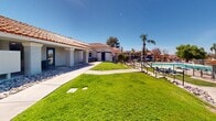 This Tucson, Arizona apartment complex showcases a harmonious blend of Southwestern architecture and modern amenities. The property boasts a series of single-story units with characteristic terracotta-tiled roofs and stucco exteriors in neutral tones. Wide, covered walkways with sturdy pillars provide shade and create inviting outdoor spaces. The landscaping is meticulously maintained, featuring expansive lawns interspersed with desert-appropriate rock gardens and native plants. A standout feature is the sparkling community pool, complete with a cabana and adjacent seating areas, perfect for relaxation and socializing. The complex also offers ample parking, including covered spaces to protect vehicles from the Arizona sun. Concrete pathways wind through the property, connecting various buildings and amenities. The overall design emphasizes open spaces and outdoor living, with generously sized patios for each unit. Palm trees and other mature vegetation add to the oasis-like atmosphere, creating a serene environment within the urban setting. The property's layout and amenities cater to a comfortable, community-oriented lifestyle in the heart of the Southwest.