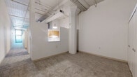 Located in the heart of downtown Cincinnati on W Fourth Street, this 1-bedroom, 1-bathroom loft blends historic architectural character with an open, industrial aesthetic. The living areas are expansive and versatile, comprising multiple defined zones that flow seamlessly into one another, all finished with plush wall-to-wall carpeting. Soaring ceilings with exposed ductwork, structural beams, and piping lend an authentic loft character, while ornate decorative columns serve as striking architectural focal points throughout the main living space. The kitchen features warm wood cabinetry and is framed by a pass-through window with pendant lighting, creating a functional yet visually connected cooking area. The bedroom is a well-proportioned private retreat, benefiting from natural light through a window and the same high-ceiling industrial design that defines the rest of the unit. A hallway connects the living spaces to the bedroom and bathroom, with an impressive five closets providing generous storage throughout. The overall ambiance is one of urban sophistication — open, airy, and full of character, ideal for those who appreciate the charm of a converted historic building in a vibrant city-center location.