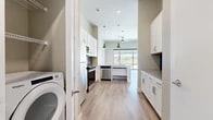 This well-appointed two-bedroom, two-bathroom residence offers a thoughtfully designed single-level layout with modern finishes throughout. Light wood-tone flooring flows seamlessly across the entire unit, complementing the soft neutral wall tones that create a clean, contemporary aesthetic.

The open-concept kitchen and living area serves as the heart of the home. The kitchen is outfitted with crisp white shaker cabinetry, quartz countertops, a blue-gray subway tile backsplash, and a full suite of stainless steel appliances including a range, microwave, dishwasher, and refrigerator. A kitchen island with pendant lighting anchors the space, while a large picture window floods the area with natural light and frames outdoor views. A ceiling fan in the living area enhances comfort and airflow.

A dedicated laundry area with an in-unit washer adds everyday convenience. The two bedrooms are generously proportioned, with the primary bedroom featuring a spacious walk-in closet with built-in shelving and hanging rods. Both bathrooms are finished with neutral tones and wood-look flooring consistent with the rest of the unit.

Large floor-to-ceiling windows in the secondary bedroom provide abundant natural light and views of the surrounding area, further enhancing the open and airy feel of this well-designed home.
