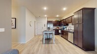 This single-floor residence offers a thoughtfully designed layout that balances comfort and functionality. The open-concept kitchen is a standout feature, showcasing rich dark-brown cabinetry, granite countertops, and a full suite of stainless steel appliances, including a refrigerator, microwave, range, and dishwasher. A center island with bar seating provides additional prep space and casual dining convenience. Light-toned wood-style flooring flows throughout the main living areas, enhancing the bright, airy atmosphere created by recessed lighting throughout.

The living room is generously sized, featuring large windows that invite natural light and provide outdoor views, creating a warm and welcoming environment. An additional flex room, also carpeted and bathed in natural light through oversized windows, offers versatile space suitable for a home office or sitting area.

The bedroom is comfortably appointed with plush carpeting, a ceiling fan, and a window with outdoor views. A walk-in closet with wire shelving provides ample storage. The primary bathroom features a dual-sink vanity with granite countertops and dark cabinetry, while a second full bathroom includes a tub-shower combination, granite countertop vanity, and matching cabinetry — both finished with consistent, cohesive design elements throughout.