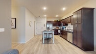 This single-floor residence offers a thoughtfully designed layout that balances comfort and functionality. The open-concept kitchen is a standout feature, showcasing rich dark-brown cabinetry, granite countertops, and a full suite of stainless steel appliances, including a refrigerator, microwave, range, and dishwasher. A center island with bar seating provides additional prep space and casual dining convenience. Light-toned wood-style flooring flows throughout the main living areas, enhancing the bright, airy atmosphere created by recessed lighting throughout.

The living room is generously sized, featuring large windows that invite natural light and provide outdoor views, creating a warm and welcoming environment. An additional flex room, also carpeted and bathed in natural light through oversized windows, offers versatile space suitable for a home office or sitting area.

The bedroom is comfortably appointed with plush carpeting, a ceiling fan, and a window with outdoor views. A walk-in closet with wire shelving provides ample storage. The primary bathroom features a dual-sink vanity with granite countertops and dark cabinetry, while a second full bathroom includes a tub-shower combination, granite countertop vanity, and matching cabinetry — both finished with consistent, cohesive design elements throughout.