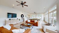 Located at 2102 Silvercrest Dr in Myrtle Beach, SC, this single-floor space exudes a relaxed coastal charm with a bright, airy aesthetic throughout. The open-concept living, dining, and kitchen area forms the heart of the space, bathed in natural light from an impressive wall of large windows and French doors that frame views of the surrounding greenery. Ceiling fans overhead and recessed lighting enhance the comfortable ambiance. The living area features light tile flooring, crown molding, and a wall-mounted TV above a decorative whitewashed sideboard, complemented by warm leather sofas and lush tropical plants. The sunlit dining area accommodates a natural wood table with woven chairs, creating an inviting setting for gatherings. The kitchen is well-appointed with rich dark wood cabinetry, granite-style countertops, and full appliances, including a side-by-side window with a peek-a-boo pool view. A welcoming entrance greets visitors with glass-paneled French doors and a round display table. The dedicated office provides a functional workspace with a long white marble-top desk, dual workstations, and nature-inspired artwork. Hallways connect each area seamlessly, ensuring a smooth and cohesive flow throughout this well-designed space.
