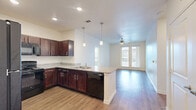 This well-appointed 2-bedroom, 3-bathroom single-story home at 1475 Gears Rd in Houston, TX offers a thoughtfully designed layout with consistent, quality finishes throughout. The open-concept kitchen and living area serves as the heart of the home, where rich dark cabinetry contrasts beautifully with granite countertops and light hardwood-style flooring. A curved kitchen peninsula with pendant lighting and an integrated sink provides additional prep space and casual seating, while recessed lighting and black appliances complete the functional kitchen design. The living room extends toward a set of French doors that open to an outdoor view, filling the space with natural light and featuring a ceiling fan overhead. The bedrooms are carpeted for comfort, with one bedroom offering direct outdoor-facing windows and ceiling fan access. Each bedroom benefits from dedicated closet space, including a walk-in closet with built-in wire shelving for generous storage. The three bathrooms are finished with matching dark cabinetry, granite-topped vanities, and hardwood-style flooring. The primary bath features an extended double vanity with a large mirror and a separate water closet, while secondary baths include tub-shower combinations framed by clean white tile. The overall palette of neutral whites and warm wood tones creates a cohesive, move-in-ready ambiance throughout.
