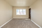 This single-floor home in Des Moines, Iowa offers a practical and efficient layout across three bedrooms, one bathroom, a kitchen, and a connecting hallway. The living area features neutral-toned carpet, built-in wall shelving, and a front-facing window that brings in natural light, with direct access to the kitchen through a warm wood-toned door. The kitchen is equipped with oak cabinetry both above and below the counters, a double stainless steel sink, white refrigerator, and durable hardwood-style flooring, with a window overlooking the exterior. The primary bedroom is the most spacious of the three, featuring carpet flooring, dual windows with natural light, a ceiling fan, and a closet. The additional bedrooms are also carpeted, each with windows and closet storage — one featuring a built-in single closet and another with double wood-paneled bi-fold doors. The bathroom includes a full tub-shower combination with white tile surround, a natural light window, a wood-vanity with countertop sink, and hardwood-style flooring. Throughout the home, warm beige walls and white trim create a clean, consistent aesthetic suited for comfortable everyday living.