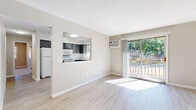 This single-floor unit offers a practical and functional layout across three bedrooms, one bathroom, a living room, kitchen, and closet. The living room is bright and airy, featuring light wood-style flooring, a textured ceiling, a wall-mounted air conditioning unit, and a baseboard heating system. A sliding glass door fills the space with natural light and opens to an outdoor deck with views of surrounding greenery.

The kitchen connects to the living area via a pass-through window, creating an open and communicative feel. It is outfitted with gray cabinetry, white appliances including a refrigerator, electric range, microwave, and dishwasher, as well as light countertops and a window over the sink for added natural light.

The bedrooms feature soft carpet flooring and baseboard heating. The primary bedroom includes a ceiling fan, two windows with outdoor views, and a closet. The secondary bedrooms are well-lit by natural light through individual windows.

The bathroom is clean and neatly finished with white tile surround, a soaking tub, a white vanity with brushed nickel hardware, a quartz-style countertop, and a mirrored medicine cabinet. Throughout the unit, neutral tones and consistent finishes contribute to a cohesive, well-maintained ambiance.
