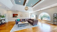 Located at 975 Westmeade Dr in Chesterfield, Missouri, this thoughtfully designed single-floor space offers a generous and open layout that balances architectural elegance with functional comfort. The main living area is immediately striking, highlighted by soaring coffered ceilings with a teal-painted inset and a statement orb chandelier that adds warmth and visual interest. Warm hardwood flooring flows seamlessly throughout the entire space, unifying each area with a cohesive, natural aesthetic.

Distinctive arched windows are a recurring architectural feature, flooding the interior with abundant natural light and offering views of the lush surrounding landscape, including a serene outdoor water feature visible from the lounge area. A floor-to-ceiling stacked stone fireplace serves as a bold focal point in the sitting area, complemented by a pair of elegant armchairs arranged for intimate conversation.

The open-concept layout accommodates a spacious main seating area, a dedicated dining space with a circular table set beneath multiple large windows, and a compact kitchen tucked in the background with rich wood cabinetry and stainless steel appliances. A quiet desk nook near a corner window provides a practical workspace. Together, these elements create a refined, welcoming atmosphere well-suited for both relaxation and gathering.