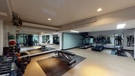 Located at 32 High Street in New Haven, CT, this fitness center offers a comprehensive, single-floor workout facility designed to accommodate a wide range of exercise needs. The space is organized into distinct workout zones, each thoughtfully equipped to support both cardio and strength training routines. The cardio area features multiple treadmills and elliptical machines, providing ample options for aerobic exercise. A mounted flat-screen television is positioned for viewing during workouts, enhancing the user experience. The strength training section is well-stocked with a full rack of dumbbells in varying weights, medicine balls, stability balls, and an adjustable weight bench, offering versatility for functional and resistance training. Additional cable and weight machines are arranged throughout the space, supporting a broad spectrum of strength exercises. Large mirrors line multiple walls, creating a sense of openness while allowing users to monitor their form. The flooring incorporates protective rubber mats in key exercise zones, ensuring safety and comfort. Recessed and fluorescent lighting illuminates the facility evenly, maintaining a clean and functional atmosphere. The neutral color palette, accented by soft teal wall tones, contributes to a focused and energizing environment suited for consistent, productive training sessions.