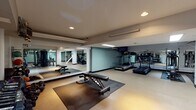 Located at 32 High Street in New Haven, CT, this fitness center offers a comprehensive, single-floor workout facility designed to accommodate a wide range of exercise needs. The space is organized into distinct workout zones, each thoughtfully equipped to support both cardio and strength training routines. The cardio area features multiple treadmills and elliptical machines, providing ample options for aerobic exercise. A mounted flat-screen television is positioned for viewing during workouts, enhancing the user experience. The strength training section is well-stocked with a full rack of dumbbells in varying weights, medicine balls, stability balls, and an adjustable weight bench, offering versatility for functional and resistance training. Additional cable and weight machines are arranged throughout the space, supporting a broad spectrum of strength exercises. Large mirrors line multiple walls, creating a sense of openness while allowing users to monitor their form. The flooring incorporates protective rubber mats in key exercise zones, ensuring safety and comfort. Recessed and fluorescent lighting illuminates the facility evenly, maintaining a clean and functional atmosphere. The neutral color palette, accented by soft teal wall tones, contributes to a focused and energizing environment suited for consistent, productive training sessions.