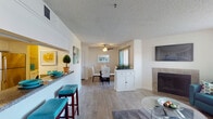 This single-floor residence offers a thoughtfully designed open-concept layout that seamlessly connects the living, dining, and kitchen areas. The living room is a comfortable focal point, featuring a tile-surround fireplace, a wall-mounted TV, and windows that invite natural light. A ceiling fan overhead adds to the airy atmosphere. Adjacent to the living area, the dining space accommodates a full table-and-chair set and flows naturally from the kitchen pass-through bar, which offers additional seating with teal upholstered barstools.

The galley-style kitchen is well-equipped with white cabinetry, granite-style countertops, stainless steel appliances including a refrigerator, microwave, and dishwasher, and a deep double-basin sink. Light wood-style flooring runs throughout the main living areas, adding warmth and cohesion.

The bedrooms are carpeted for comfort, each offering ample natural light through large windows with sheer curtains. The primary bedroom connects to a vanity area with dual sinks and granite-style countertops, while the full bathroom features a tub-shower combination with white tile surround and white cabinetry. The textured ceilings are consistent throughout, contributing to the residence's classic interior character.