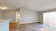 This single-floor residence showcases a thoughtfully designed layout with a mix of hardwood-style and carpeted flooring throughout. The main living area immediately impresses with dramatic vaulted ceilings that lend an expansive, airy feel to the space. Neutral grey-toned walls complement the warm wood flooring, creating a clean and inviting atmosphere. A sliding glass door fills the living area with natural light and provides direct access to an outdoor deck, enhancing the connection between interior and exterior spaces.

The galley-style kitchen is well-equipped, featuring crisp white cabinetry, marble-look countertops, and black appliances including a refrigerator, dishwasher, and range. An adjacent utility area provides added convenience with in-unit laundry access.

Bedrooms are finished with plush carpeting and ceiling fans, offering a comfortable retreat. The primary bedroom benefits from dual closets with built-in shelving, providing generous storage. The bathroom is finished with wood-style flooring, a white vanity with marble-look countertops, and brushed nickel fixtures. A half-wall detail near the upper-level hallway adds an architectural element, contributing to the overall cohesive and modern design of the home.