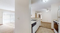 Located in Wilmington, Ohio, this single-floor residence offers a practical and comfortable layout designed for everyday living. The kitchen is efficiently arranged with white cabinetry, a double-basin sink, a dishwasher, a range, and a refrigerator, complemented by a breakfast bar that opens toward the dining area. Tile flooring in the kitchen transitions to neutral carpeting that extends throughout the living spaces and bedrooms, adding warmth underfoot. The spacious living room is a standout feature, bathed in natural light through a large sliding glass door dressed with vertical blinds, creating a bright and airy atmosphere. A ceiling fan adds comfort to the adjoining dining area. The bedrooms are generously sized with plush carpeting, ample wall space, and windows fitted with blinds to control natural light. The unit includes two full bathrooms, each appointed with a single-sink vanity with wood-accented cabinetry, a tub-shower combination with a marble-style surround, and tile flooring. A built-in vanity area with a large mirror and storage drawers provides additional convenience. Textured ceilings are found throughout, and the overall palette of whites and warm neutrals gives the space a clean, move-in-ready feel.
