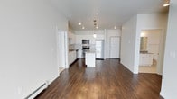 This single-floor residence offers a clean, contemporary design with an open-concept living and kitchen area that creates a bright and airy atmosphere. The kitchen is a standout feature, outfitted with crisp white cabinetry, stainless steel appliances including a refrigerator, built-in microwave, and a double oven range. A central island provides additional prep space and serves as a natural gathering point, while a classic pendant light fixture adds a polished finishing touch above it. A subtle tile backsplash accents the cooking area, complementing the light stone countertops. Recessed lighting throughout keeps the space well-illuminated and modern. Rich, dark hardwood-style flooring extends across the open living area, offering a warm contrast to the bright white walls and cabinetry. The layout flows seamlessly, with doorways leading to additional rooms, offering practical connectivity throughout the residence. The overall ambiance is fresh, functional, and move-in ready, with a neutral palette that provides a versatile backdrop for a variety of interior styles. The space is well-suited for those seeking a modern, low-maintenance living environment with thoughtful design details.