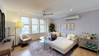 This thoughtfully designed single-floor residence offers a cohesive blend of contemporary finishes and warm, inviting interiors throughout its well-appointed spaces. The living room serves as the heart of the home, anchored by large roller-shade windows that frame treetop views and flood the room with natural light. Warm hardwood flooring, crown moulding, a ceiling fan, and a wall-mounted split air conditioning unit contribute to both comfort and style. A soft lavender feature wall provides a calming backdrop to the generous sectional sofa, glass-topped coffee table, and a curated gallery of framed artwork.

The kitchen is a standout space, showcasing deep navy cabinetry with under-cabinet lighting, a white stone waterfall island with seating for three, a stainless steel range hood, and a classic tile backsplash — a striking combination of bold and refined elements.

The primary bedroom features a rich, deep purple accent wall, ceiling fan, and in-unit stacked laundry conveniently positioned nearby. A second bedroom maintains a bright, neutral palette with a window overlooking the treetops and its own split AC unit. The bathroom impresses with floor-to-ceiling marble-effect tile, a glass-enclosed walk-in shower with a built-in bench, and a sleek modern vanity.