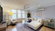 This thoughtfully designed single-floor residence offers a cohesive blend of contemporary finishes and warm, inviting interiors throughout its well-appointed spaces. The living room serves as the heart of the home, anchored by large roller-shade windows that frame treetop views and flood the room with natural light. Warm hardwood flooring, crown moulding, a ceiling fan, and a wall-mounted split air conditioning unit contribute to both comfort and style. A soft lavender feature wall provides a calming backdrop to the generous sectional sofa, glass-topped coffee table, and a curated gallery of framed artwork.

The kitchen is a standout space, showcasing deep navy cabinetry with under-cabinet lighting, a white stone waterfall island with seating for three, a stainless steel range hood, and a classic tile backsplash — a striking combination of bold and refined elements.

The primary bedroom features a rich, deep purple accent wall, ceiling fan, and in-unit stacked laundry conveniently positioned nearby. A second bedroom maintains a bright, neutral palette with a window overlooking the treetops and its own split AC unit. The bathroom impresses with floor-to-ceiling marble-effect tile, a glass-enclosed walk-in shower with a built-in bench, and a sleek modern vanity.