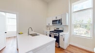 Located at 441 W Main St in Cary, Illinois, this thoughtfully laid-out 2-bedroom, 1-bathroom residence offers a clean, modern aesthetic across a single floor. The open-concept kitchen and dining area serves as the heart of the home, featuring crisp white shaker cabinetry with matte black hardware, bright white quartz countertops, a central island with a double undermount sink, and a full suite of stainless steel appliances including a gas range, over-the-range microwave, and French door refrigerator. Soaring ceilings in the kitchen amplify the sense of space, while large windows invite generous natural light and views of the surrounding neighborhood. Warm, light-toned hardwood-style flooring flows consistently throughout the home, adding cohesion and character to every room. Both bedrooms are bright and comfortable, each benefiting from natural light through well-placed windows with outdoor views of mature trees. The full bathroom is elegantly finished with a dual-sink white vanity, gold-toned fixtures, classic subway tile surrounding the tub-shower combination, and wood-look tile flooring. A dedicated closet and entrance area complete this well-appointed, move-in-ready residence in the heart of Cary, IL.