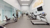This fitness center in Jacksonville, FL offers a comprehensive, single-floor exercise facility designed to support a wide range of workout routines. The main workout area is bright and welcoming, featuring warm orange accent walls, crown molding, and an abundance of large windows that flood the space with natural light and provide views of the surrounding greenery. French doors open directly to the outdoors, enhancing the airy atmosphere.

The cardio section is well-stocked with multiple treadmills, elliptical trainers, a stationary bike, and a rowing machine, all arranged to take full advantage of the natural light and outdoor views. A wall-mounted flat-screen television is positioned for easy viewing during workouts. The strength training area includes a multi-station weight machine, a dumbbell rack, and various benches, complemented by a large floor-to-ceiling mirror that visually expands the space. Rubber flooring throughout provides both safety and durability.

An accessible unisex restroom is conveniently located within the facility. A dedicated children's play nook features a colorful patterned carpet, small chairs, a toy storage unit, and a wall-mounted television, making the fitness center family-friendly. Recessed lighting and crown molding throughout add a polished, finished look to the overall space.