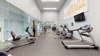 This fitness center in Jacksonville, FL offers a comprehensive, single-floor exercise facility designed to support a wide range of workout routines. The main workout area is bright and welcoming, featuring warm orange accent walls, crown molding, and an abundance of large windows that flood the space with natural light and provide views of the surrounding greenery. French doors open directly to the outdoors, enhancing the airy atmosphere.

The cardio section is well-stocked with multiple treadmills, elliptical trainers, a stationary bike, and a rowing machine, all arranged to take full advantage of the natural light and outdoor views. A wall-mounted flat-screen television is positioned for easy viewing during workouts. The strength training area includes a multi-station weight machine, a dumbbell rack, and various benches, complemented by a large floor-to-ceiling mirror that visually expands the space. Rubber flooring throughout provides both safety and durability.

An accessible unisex restroom is conveniently located within the facility. A dedicated children's play nook features a colorful patterned carpet, small chairs, a toy storage unit, and a wall-mounted television, making the fitness center family-friendly. Recessed lighting and crown molding throughout add a polished, finished look to the overall space.