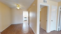 This single-story unit is designed with a practical, straightforward layout finished in warm beige tones throughout. The living area is generously sized, featuring plush carpet flooring, a textured ceiling, and a front entry door with gold hardware. Natural light enters through a large window, creating a bright and open atmosphere. Ceiling fans with light fixtures are installed in the living area and multiple bedrooms, providing both air circulation and ambient lighting.

The kitchen is equipped with white cabinetry, a full-size refrigerator, dishwasher, countertop workspace, and a stainless steel double sink positioned beneath a window that allows natural light. Wood-look flooring runs through the kitchen and hallway areas, providing a cohesive transition between spaces.

The bedrooms are carpeted, each featuring windows for natural light and ceiling fans. The rooms offer ample wall space and are well-suited for varied furniture arrangements. HVAC vents are present throughout for climate control.

Two full bathrooms include tub/shower combinations with white tile surrounds, white vanities with integrated sinks, large mirrors, and wood-look flooring. The overall unit presents a clean, functional living environment with consistent finishes throughout.
