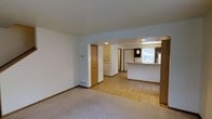 This multi-floor space is designed with practicality and open-concept living in mind. The main level showcases a seamless transition between the living area and the kitchen, creating a cohesive and versatile floor plan. The living area is finished with plush carpeting, while the adjacent spaces feature light hardwood-style flooring that adds warmth and continuity throughout. A peninsula-style breakfast bar defines the kitchen area, providing both workspace and casual seating options. The kitchen is well-lit with overhead lighting and features a window that allows natural light to fill the space. A dedicated laundry area with stacked or side-by-side units is conveniently located just off the main living space, adding to the home's functionality. Interior doors with warm wood-toned finishes complement the neutral white walls and light-colored trim, lending a clean and classic aesthetic throughout. Recessed lighting and pendant fixtures provide layered illumination across the common areas. Spanning three floors, this space offers ample room for a variety of living arrangements, making it a well-rounded and highly functional home for everyday living.