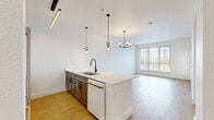 Located at 6851 S Gaylord St in Centennial, CO, this thoughtfully designed 2-bedroom, 1-bathroom unit offers a clean, modern aesthetic across a well-utilized single floor. The open-concept kitchen and living area serves as the heart of the home, anchored by a large peninsula with striking white quartz countertops and an undermount sink with a matte black faucet. The kitchen features two-tone cabinetry — white upper cabinets paired with rich wood-toned lower cabinets — alongside stainless steel appliances and stylish pendant lighting that adds warmth and character. Light wood-tone flooring flows throughout the entire unit, creating a cohesive and inviting feel. The living area benefits from large windows that draw in generous natural light, with access to an exterior door for added convenience. A bright hallway connects the living spaces to the bedrooms, both of which are well-proportioned and feature large windows with vertical blinds, offering ample daylight. The full bathroom is finished to a high standard, showcasing a glass-enclosed walk-in shower with white tile surround, matte black hardware, and a wood-toned vanity with white countertop. A dedicated utility room and two closets provide practical storage solutions throughout this clean, contemporary home.