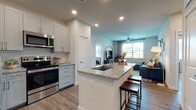 This well-appointed single-floor residence offers a thoughtfully designed open-concept layout that seamlessly connects the kitchen, dining, and living areas. The kitchen is a standout feature, showcasing white shaker-style cabinetry that extends to the ceiling, granite countertops, stainless steel appliances including a French door refrigerator, electric range, microwave, and dishwasher, and a large center island with a built-in sink and bar seating — ideal for both meal prep and casual dining. Wood-look flooring runs throughout the space, adding warmth and continuity.

The living area is bright and comfortable, benefiting from natural light through large windows and a ceiling fan overhead. The bedrooms are well-sized, each offering windows with outdoor views and wood-look flooring. One bedroom includes a dedicated desk nook, providing a functional workspace within the room.

The primary ensuite bathroom features a dual-sink vanity with granite countertops, gray cabinetry, a large mirror with overhead lighting, and direct access to an adjoining bedroom. A generously sized walk-in closet with multi-tiered wire shelving and hanging rods provides ample storage. Recessed lighting throughout the residence ensures a clean, modern aesthetic.
