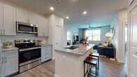 This well-appointed single-floor residence offers a thoughtfully designed open-concept layout that seamlessly connects the kitchen, dining, and living areas. The kitchen is a standout feature, showcasing white shaker-style cabinetry that extends to the ceiling, granite countertops, stainless steel appliances including a French door refrigerator, electric range, microwave, and dishwasher, and a large center island with a built-in sink and bar seating — ideal for both meal prep and casual dining. Wood-look flooring runs throughout the space, adding warmth and continuity.

The living area is bright and comfortable, benefiting from natural light through large windows and a ceiling fan overhead. The bedrooms are well-sized, each offering windows with outdoor views and wood-look flooring. One bedroom includes a dedicated desk nook, providing a functional workspace within the room.

The primary ensuite bathroom features a dual-sink vanity with granite countertops, gray cabinetry, a large mirror with overhead lighting, and direct access to an adjoining bedroom. A generously sized walk-in closet with multi-tiered wire shelving and hanging rods provides ample storage. Recessed lighting throughout the residence ensures a clean, modern aesthetic.