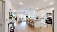 Located in Orlando, FL, this well-appointed 2-bedroom, 3-bathroom single-story home offers a thoughtfully designed open-concept layout with modern finishes throughout. The kitchen is a standout feature, showcasing crisp white shaker cabinetry, granite countertops, stainless steel appliances including a side-by-side refrigerator, electric range, and built-in microwave, complemented by a tile backsplash and pendant lighting over a breakfast bar with seating. Light wood-style flooring flows seamlessly from the kitchen into the living room, which is bathed in natural light from large windows and a glass door opening to an outdoor area with views of greenery. Both bedrooms are generously sized and carpeted, each featuring ceiling fans, natural light from dual windows, and dedicated closets — including a spacious walk-in closet with built-in shelving. The primary bath offers a dual-sink granite vanity with white cabinetry and a glass-enclosed walk-in shower with full-height tile surround. Additional bathrooms provide further convenience. A dedicated utility room rounds out this functional and attractively finished home.