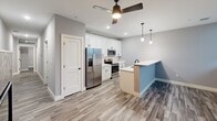 Located at 1230 Elm St in Manchester, NH, this two-bedroom, one-bathroom unit offers a well-designed, single-floor layout with a thoughtful mix of hard flooring and soft carpeting throughout. The open kitchen is a standout feature, equipped with stainless steel appliances including a French door refrigerator, electric range, and built-in microwave. Crisp white shaker-style cabinetry pairs with a light countertop peninsula, ideal for casual dining or meal prep. A ceiling fan with integrated lighting and recessed fixtures illuminate the space, while pendant lights above the peninsula add a modern touch. The kitchen flows into the main living area, finished with durable wood-look plank flooring in a neutral tone. Both bedrooms are carpeted with a patterned grey finish and feature clean, grey-toned walls with white trim. The primary bedroom offers a comfortable footprint, while the second bedroom includes a closet with wire shelving. The bathroom is well-appointed with a white vanity, quartz-style countertop, black hardware accents, and a large mirror. A notable convenience is the in-unit stacked washer and dryer tucked into a dedicated niche within the bathroom. A hallway connects all rooms efficiently, completing this functional and modern residential layout.