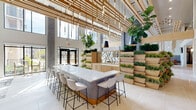 Located at 1001 Compass Way in Newark, Delaware, this single-floor amenity space showcases a sophisticated biophilic design philosophy that seamlessly blends natural elements with contemporary architecture. The space is defined by its soaring double-height ceilings, from which cascading wood slat installations and elegant pendant lighting descend, creating a dramatic yet warm visual canopy throughout.

A central feature of the space is a striking tiered living wall system constructed from light wood, filled with lush greenery that adds vibrancy and a sense of organic life to the interior. Large-format porcelain tile flooring in soft neutral tones runs throughout, reinforcing the clean, modern aesthetic. Floor-to-ceiling windows flood the space with abundant natural light while offering direct views of an outdoor courtyard and pool area.

The layout accommodates a variety of functional zones. A generously sized white quartz bar-height communal table with contemporary seating serves as a co-working and social hub. Comfortable lounge seating areas feature upholstered chairs and organic accent tables. A dedicated recreation area includes a full pool table, wall-mounted television, and casual seating. Intimate curved banquette booths provide semi-private gathering spots, while a spacious open lounge with oversized windows offers serene poolside views. The overall ambiance is welcoming, modern, and thoughtfully curated.