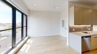 Located on the fifth floor at 1525 N American St in Philadelphia's vibrant Northern Liberties neighborhood, Unit 521 is a thoughtfully designed studio that maximizes every inch of its compact footprint. The open-plan layout connects the living area to a well-appointed galley kitchen, creating a cohesive and functional living space throughout.

The kitchen is a standout feature, showcasing a contemporary two-tone design with warm wood-finish upper cabinetry on one side and crisp white cabinetry on the other. Sleek gray quartz countertops run the length of both walls, complemented by stainless steel appliances including a range, refrigerator, dishwasher, and built-in microwave. Under-cabinet lighting adds a refined touch, while light hardwood flooring runs seamlessly through the entire unit.

The open living area benefits from a large floor-to-ceiling window with black framing, flooding the space with natural light and offering views of the surrounding cityscape. Recessed lighting and clean white walls enhance the bright, airy atmosphere.

The bathroom features a clean, modern aesthetic with warm golden floor tiles, two-tone wall tiling in the tub/shower surround, and a floating wood-finish vanity. The overall design of the unit reflects a consistent modern sensibility, making it an efficient and stylish urban residence.