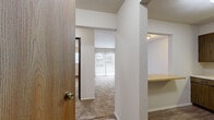 Located at 1819 N. 5th St. in Niles, Michigan, this one-bedroom, one-bathroom unit offers a practical and efficiently organized single-floor layout. The entrance opens into a hallway that connects the main living areas, with a built-in counter shelf marking the transition between the kitchen and living spaces. The living room is carpeted and bathed in natural light through a large sliding glass door fitted with vertical blinds, which leads to an outdoor area. A wall-mounted air conditioning unit provides climate control in this space. The kitchen features dark wood cabinetry extending to the upper walls, a double-basin sink, a white electric coil range, and wood-look vinyl flooring, offering ample storage and a functional workspace. The bedroom is a well-proportioned, carpeted room with a ceiling fan and light fixture, a window with exterior views, and baseboard heating. A closet is accessible directly from the bedroom. The bathroom includes a full tub-shower combo with a molded surround, a toilet, and a vanity, finished with wood-look vinyl flooring. Baseboard heating is present throughout the unit, ensuring consistent warmth. The overall aesthetic is clean and straightforward, with neutral tones and practical finishes throughout.