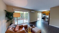 Located at 235 Acalanes Dr in Sunnyvale, CA, this single-story residence presents a well-designed, open layout with consistent dark hardwood-style flooring connecting the main living areas. The living room serves as the heart of the home, featuring multiple large sliding glass doors that flood the space with natural light and provide direct access to a private outdoor patio. Greenery visible through the glass creates a seamless indoor-outdoor connection. A wall-mounted mini-split system ensures year-round climate comfort. The kitchen is thoughtfully appointed with warm-toned wood cabinetry extending to the ceiling, a clean white countertop, and a full suite of stainless steel appliances including a range, microwave, dishwasher, and refrigerator. A sliding glass door in the kitchen offers additional outdoor access and natural light. The bedroom features soft carpeting, neutral walls, and a window with vertical blinds allowing adjustable natural light. The bathroom is finished with a wood-toned vanity, white countertop, large mirror, glass-enclosed walk-in shower, and dark hardwood-style flooring, maintaining a cohesive aesthetic throughout the home.