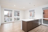 This single-floor unit showcases a contemporary, open-concept design with a cohesive neutral palette and light hardwood flooring throughout. The kitchen serves as the centerpiece of the space, featuring a generously sized island with a crisp white quartz countertop, an undermount sink, and dark espresso cabinetry beneath. Pendant lights hang above the island, adding both function and style. The full kitchen wall houses stainless steel appliances, including a French door refrigerator, a range, and a microwave, complemented by a subway tile backsplash and a mix of dark and light wood upper cabinetry. Multiple large windows flood the kitchen and living areas with natural light while offering views of the surrounding urban landscape. The open layout, visible in the 3D floor plan, reveals a well-proportioned living area adjacent to the kitchen. The bathroom features a wide-format mirror, a white quartz vanity with dark cabinetry, a subway-tiled tub-shower combination, and chrome fixtures for a clean, modern finish. A dedicated walk-in closet provides ample storage with multi-tiered shelving and hanging rods. Overall, the unit presents a bright, well-appointed living environment suited to modern urban living.