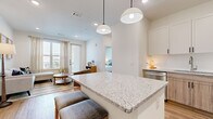 This well-designed one-bedroom, one-bathroom unit makes efficient use of its compact footprint across a single floor. The open-plan kitchen and living area forms the heart of the space, anchored by a granite-topped island with bar seating illuminated by two pendant lights overhead. The kitchen features a two-tone cabinet design—white upper cabinetry paired with warm wood-toned lower cabinets—complemented by a white tile backsplash, under-cabinet lighting, and a full suite of stainless steel appliances including a dishwasher, range, microwave, and refrigerator. Light hardwood-style flooring runs throughout, contributing to a cohesive, airy aesthetic. The living area benefits from multiple windows and a private exterior door, allowing natural light to fill the space. The bedroom is a calm, understated retreat with a large window framing outdoor views. It connects to a dedicated walk-in closet outfitted with built-in shelving, hanging rods, and organizational storage. The bathroom features a granite-topped vanity with white shaker cabinets, a large mirror, and hardwood-style flooring, with direct access to the bedroom reinforcing a practical layout throughout.